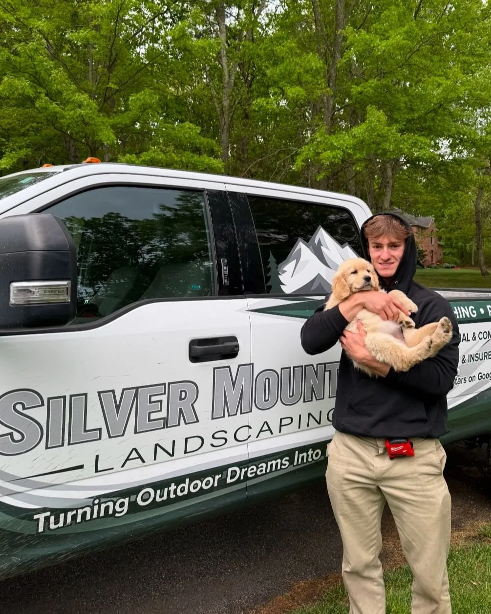Nicholas, owner of Silver Mountain Landscaping, holding a golden retriever puppy beside the company truck