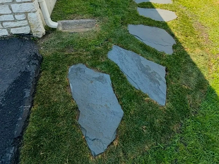 Irregular bluestone stepping stones set into freshly laid sod beside a house and driveway